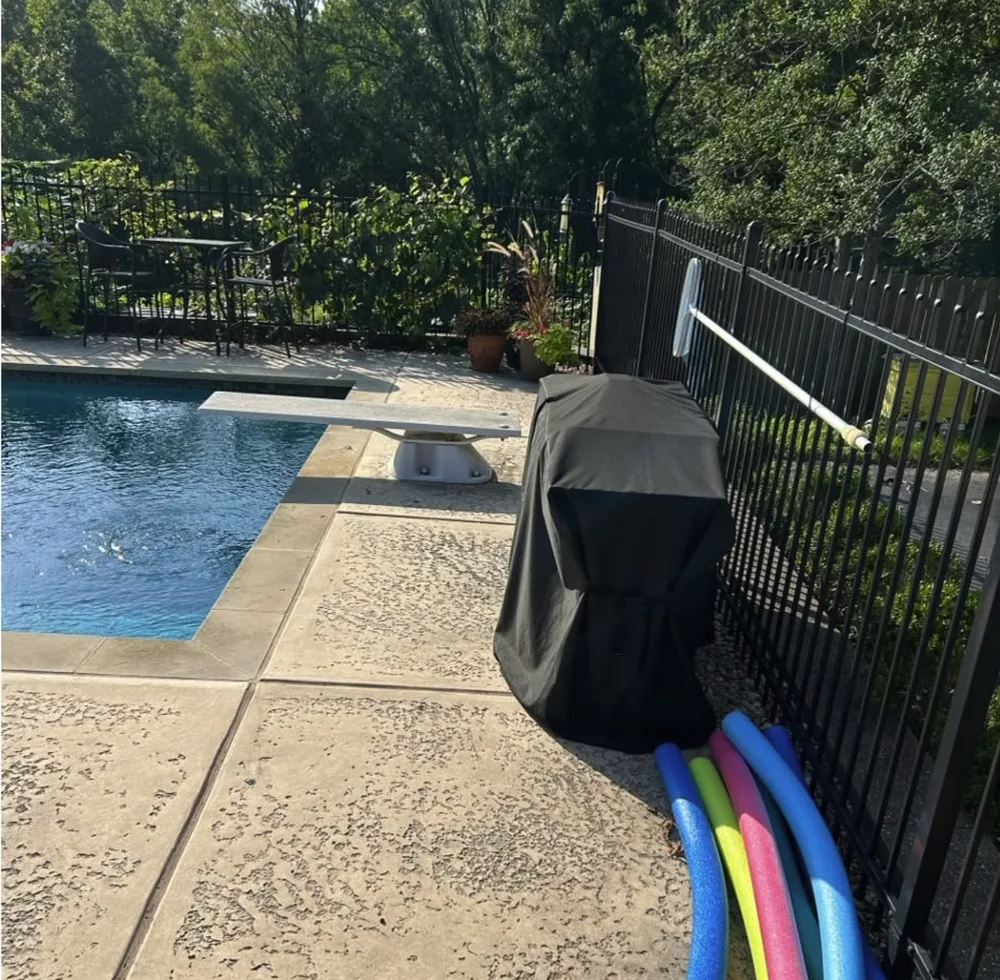 Stamped concrete pool deck dark with grime before cleaning, diving board in the background